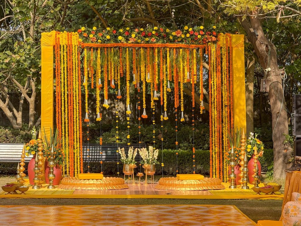 The haldi focal stage: marigold strings, white bead tassels and paired lotus-shaped seating.