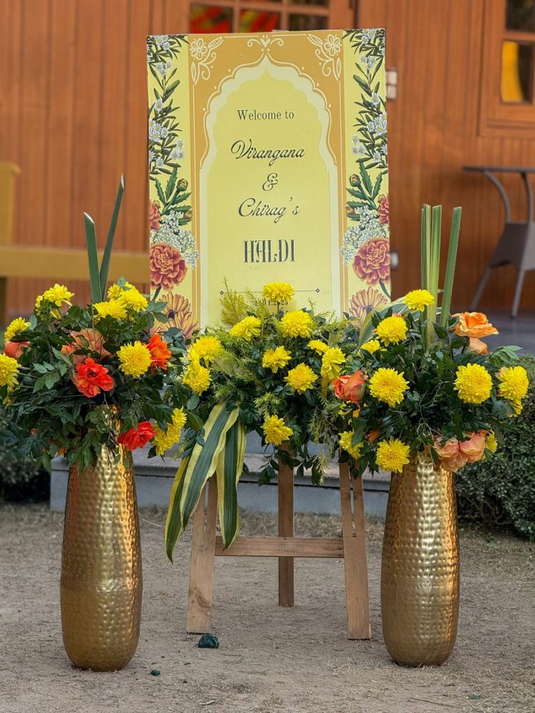 Virangana and Chirag’s haldi welcome sign, framed by yellow flowers.