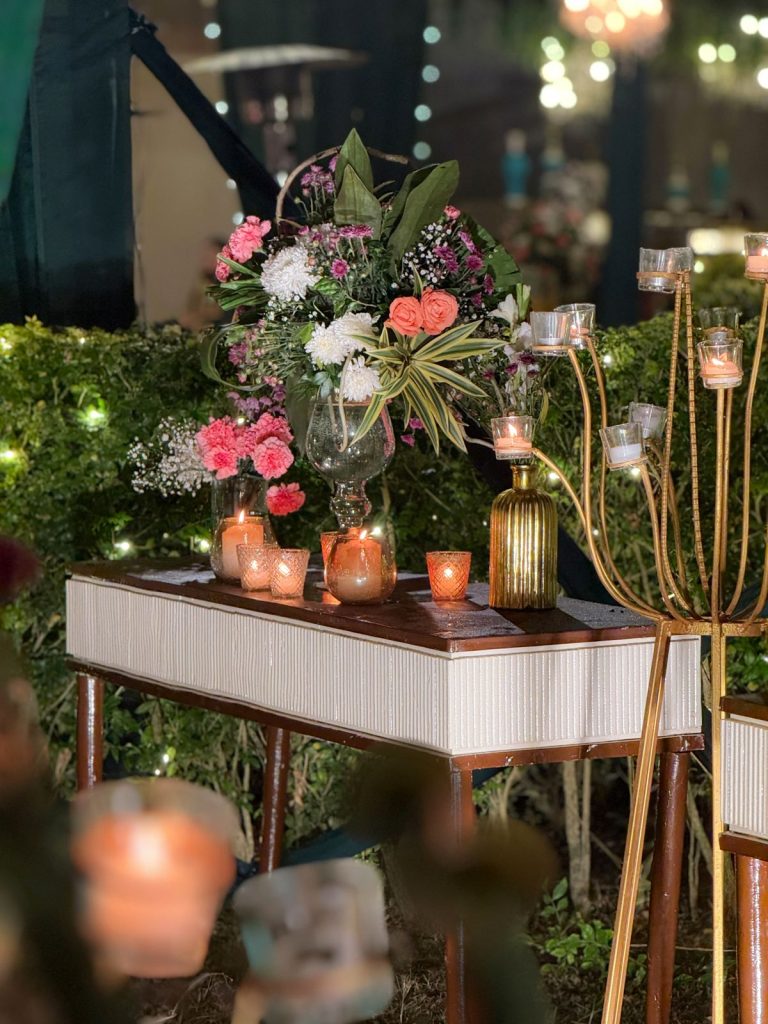 Flowers and lit candles on a console beside the sangeet arrival route.