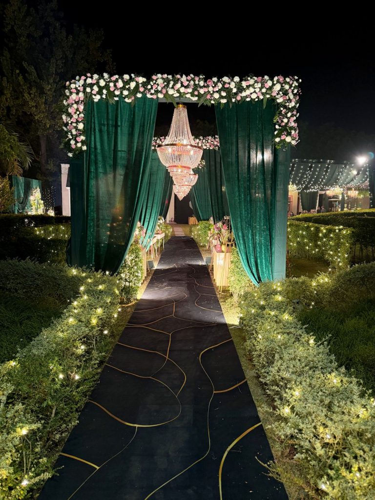 A green-draped arrival corridor lined with chandeliers and flowers.