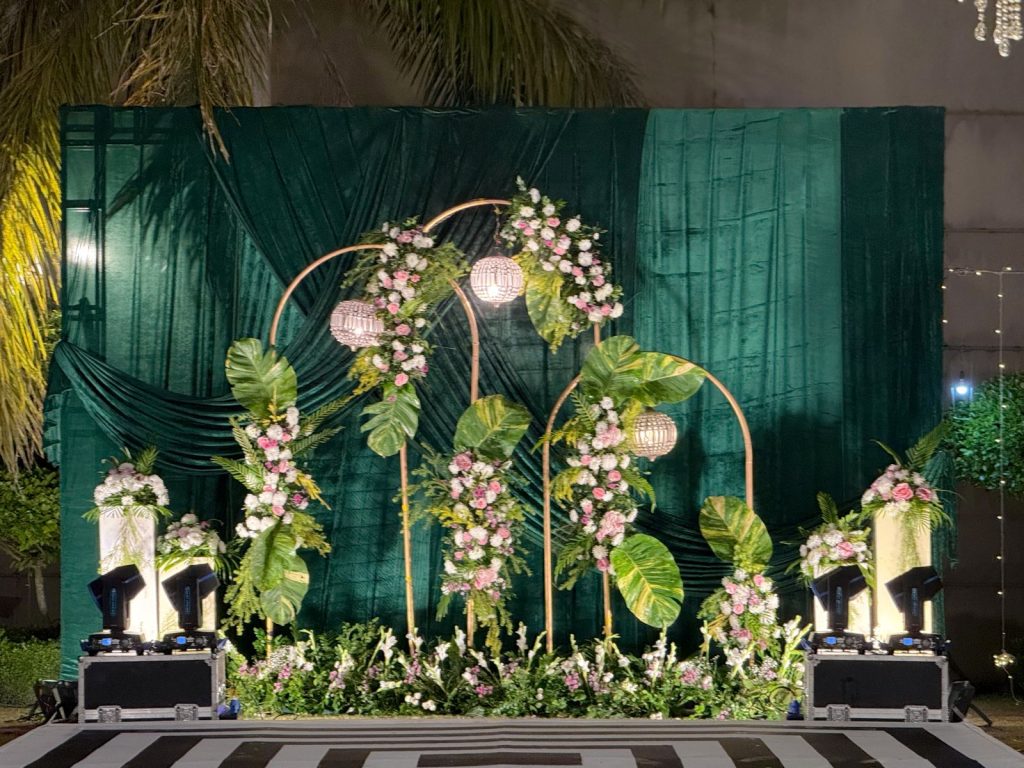 The full sangeet focal backdrop, with floral frames, suspended lights and the geometric floor in front.