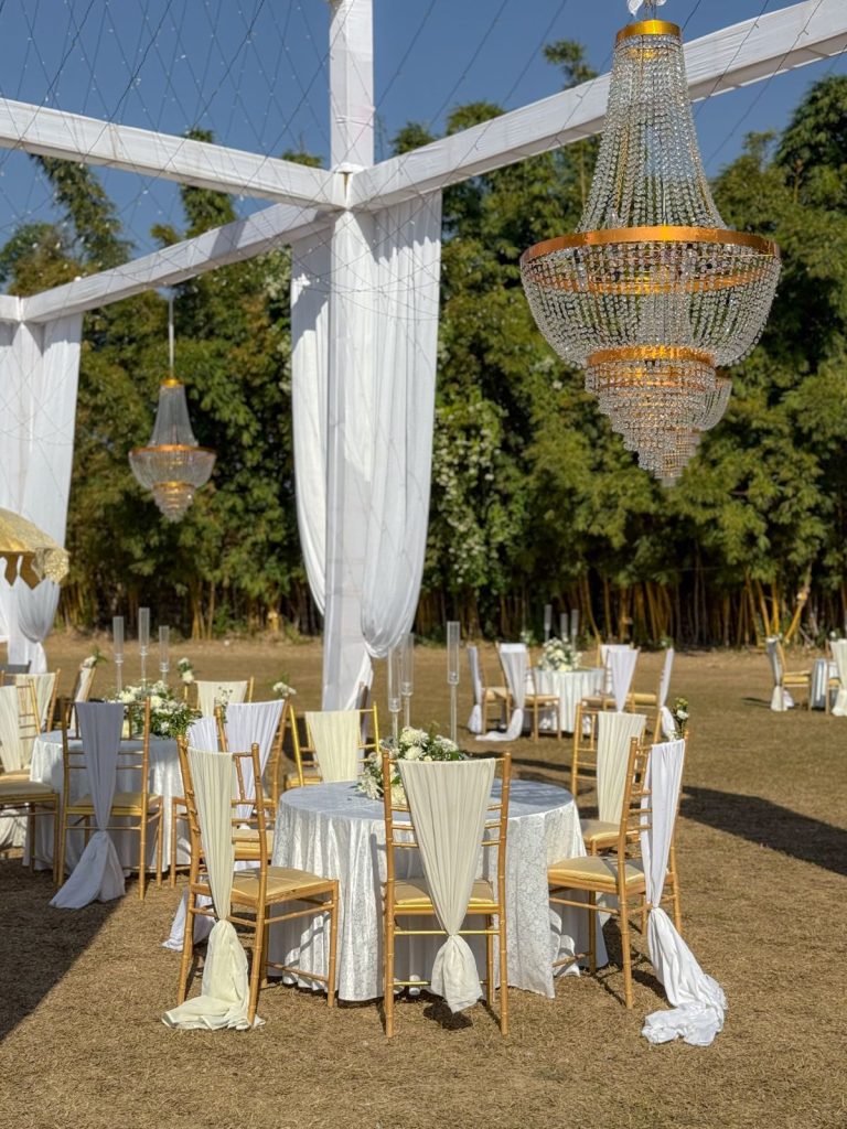 White-draped frames, chandeliers and round tables on the lawn.
