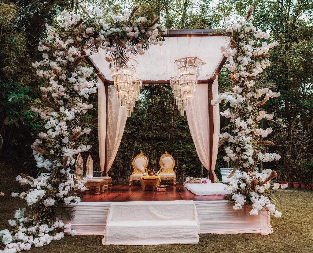 Ivory drapes, white flowers and tiered chandeliers framing Niharika and Anirudh’s garden mandap
