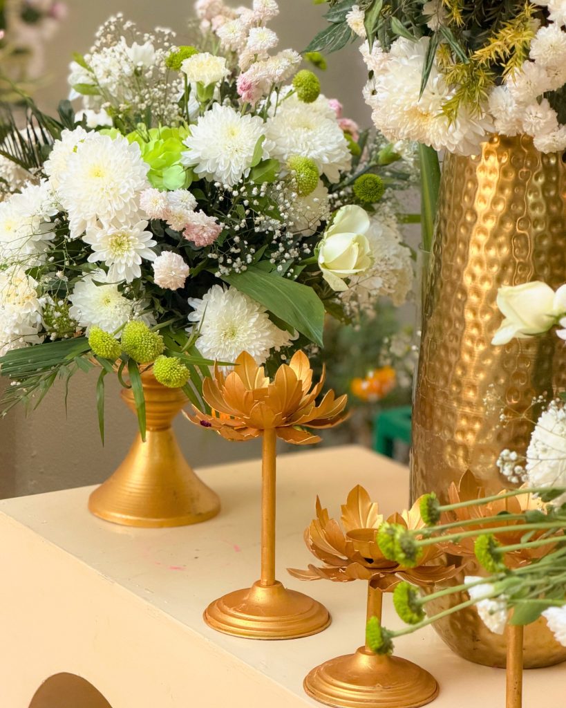 White flowers in gold vessels beside lotus-shaped decor stands